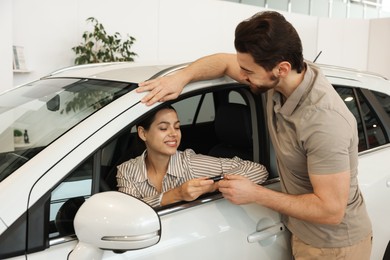 Photo of Happy husband giving key to his wife inside new car in salon