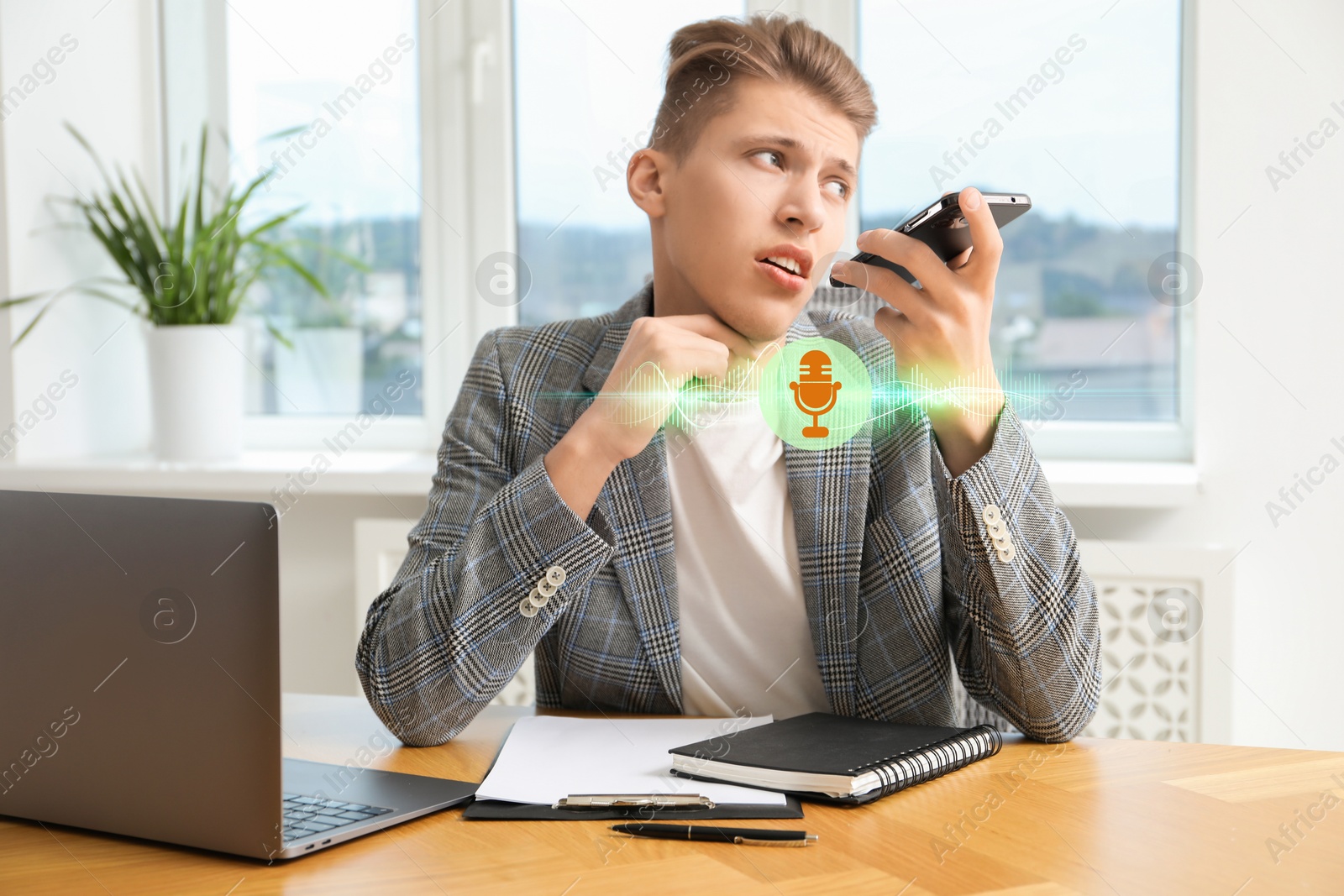 Image of Young man recording voice message via smartphone in office. Illustration of microphone and sound waves