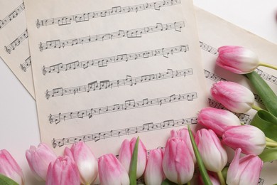 Photo of Beautiful tulips and sheets with music notes on white table, flat lay