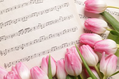 Photo of Beautiful tulips on sheets with music notes, top view