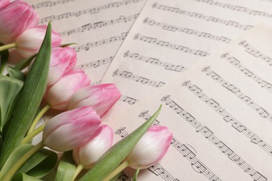 Photo of Beautiful tulips on sheets with music notes, closeup