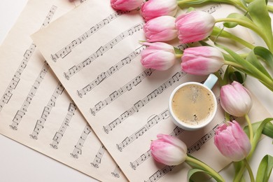 Photo of Beautiful tulips, cup of coffee and sheets with music notes on white table, flat lay