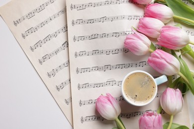 Beautiful tulips, cup of coffee and sheets with music notes on white table, flat lay