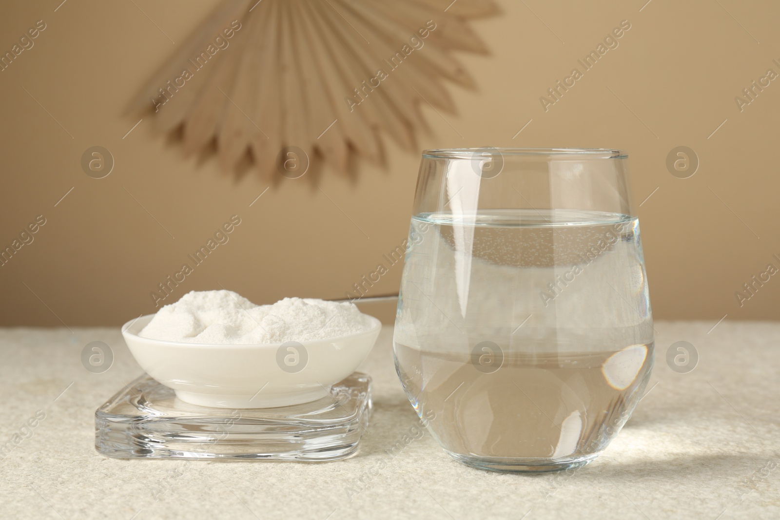 Collagen powder in bowl and glass of water on light textured table against beige background, closeup Photo of Collagen powder in bowl and glass of water on light textured table against beige background, closeup