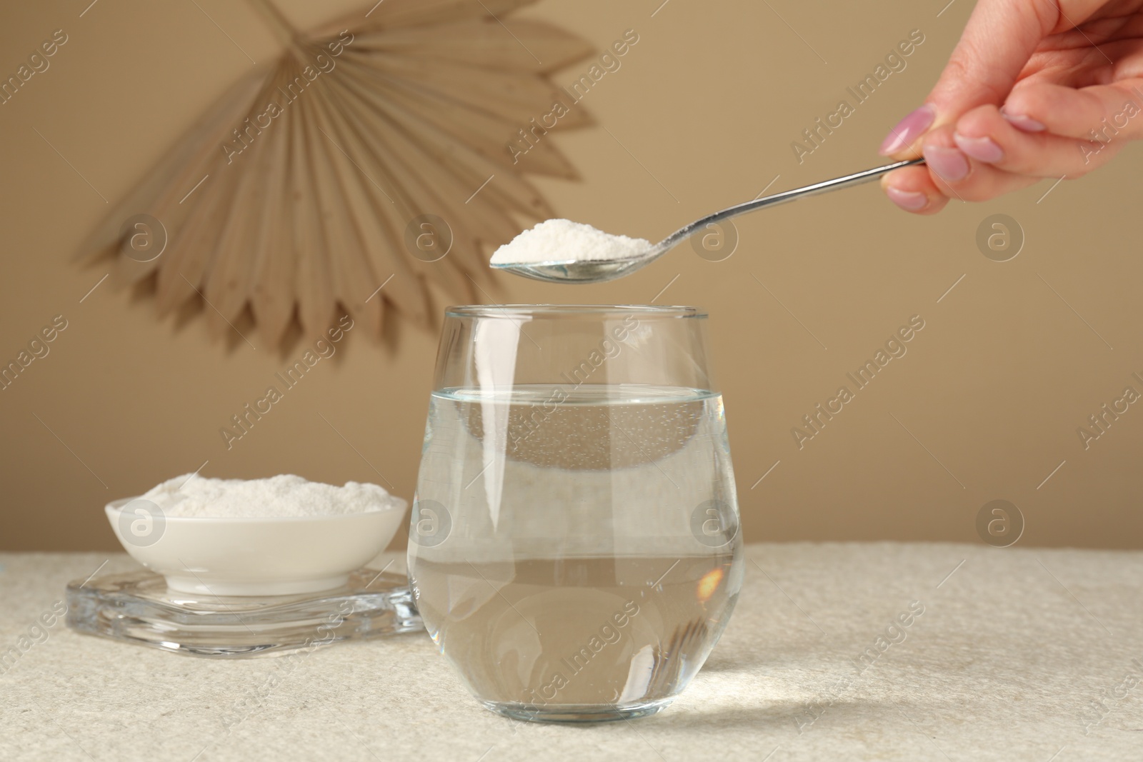 Woman adding collagen powder into glass with water at light textured table against beige background, closeup Photo of Woman adding collagen powder into glass with water at light textured table against beige background, closeup