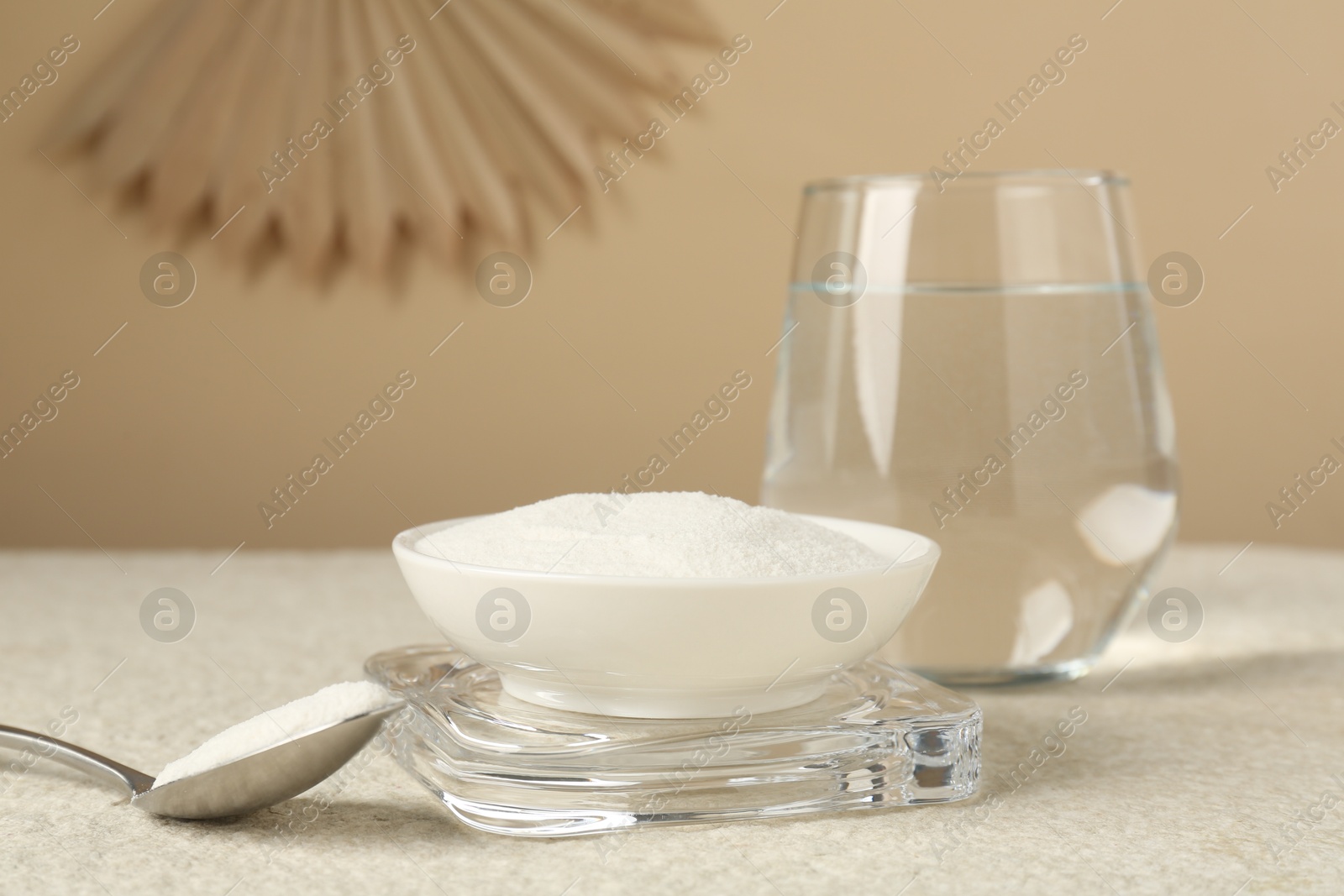 Collagen powder in bowl, spoon and glass of water on light textured table against beige background, closeup Photo of Collagen powder in bowl, spoon and glass of water on light textured table against beige background, closeup