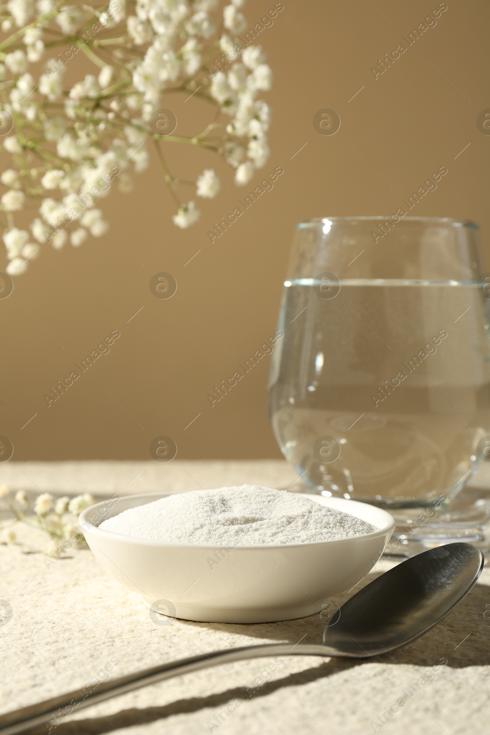 Collagen powder in bowl, spoon, glass of water and gypsophila branches on light textured table against beige background, closeup Photo of Collagen powder in bowl, spoon, glass of water and gypsophila branches on light textured table against beige background, closeup