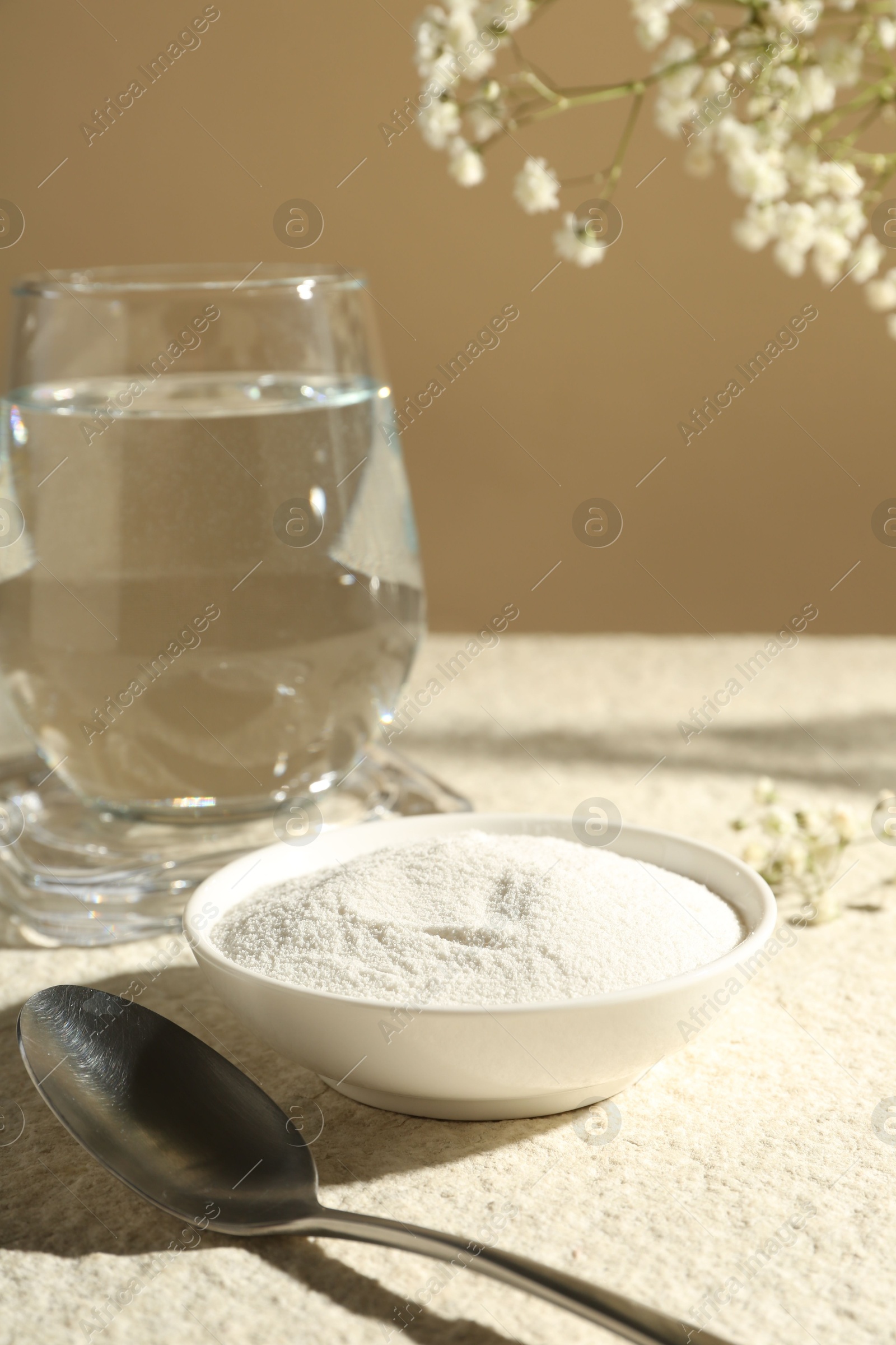 Collagen powder in bowl, spoon, glass of water and gypsophila branches on light textured table against beige background, closeup Photo of Collagen powder in bowl, spoon, glass of water and gypsophila branches on light textured table against beige background, closeup