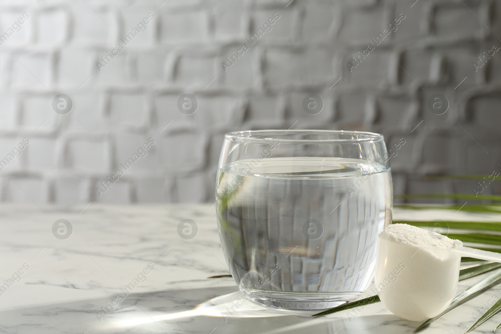 Collagen powder in scoop and glass of water on light marble table, space for text Photo of Collagen powder in scoop and glass of water on light marble table, space for text