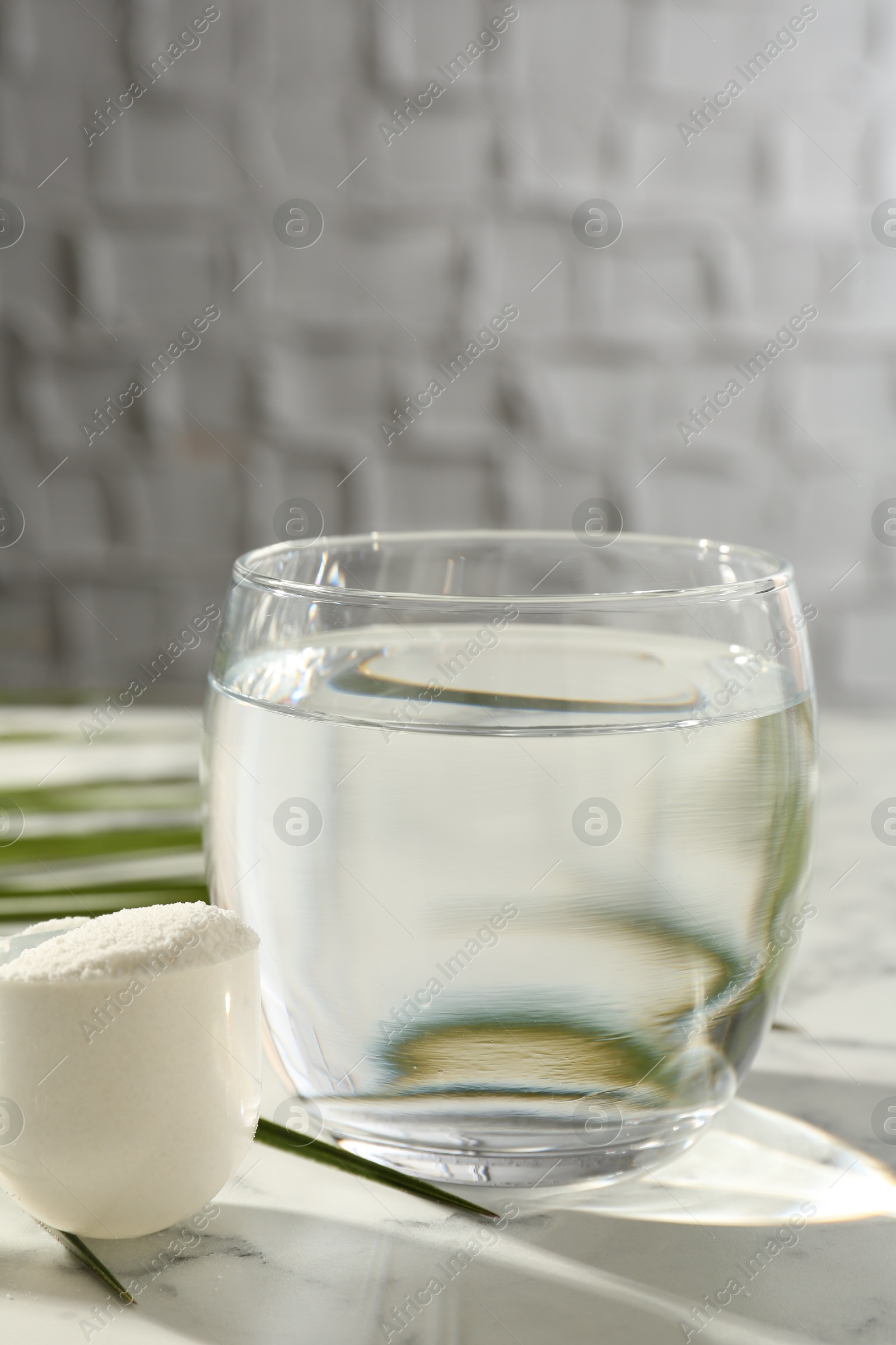 Collagen powder in scoop and glass of water on light marble table Photo of Collagen powder in scoop and glass of water on light marble table