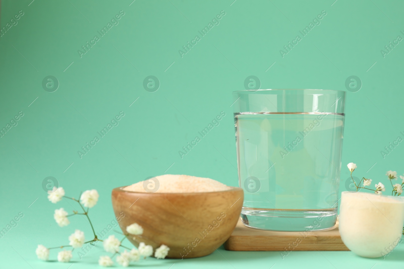 Collagen powder in bowl, scoop, glass of water and gypsophila flowers on turquoise background Photo of Collagen powder in bowl, scoop, glass of water and gypsophila flowers on turquoise background