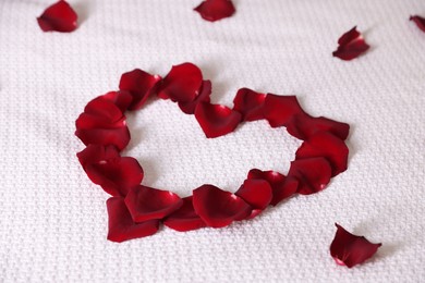 Photo of Heart made with beautiful rose petals on bed, closeup
