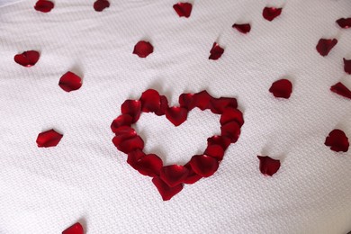 Photo of Heart made with beautiful rose petals on bed, above view