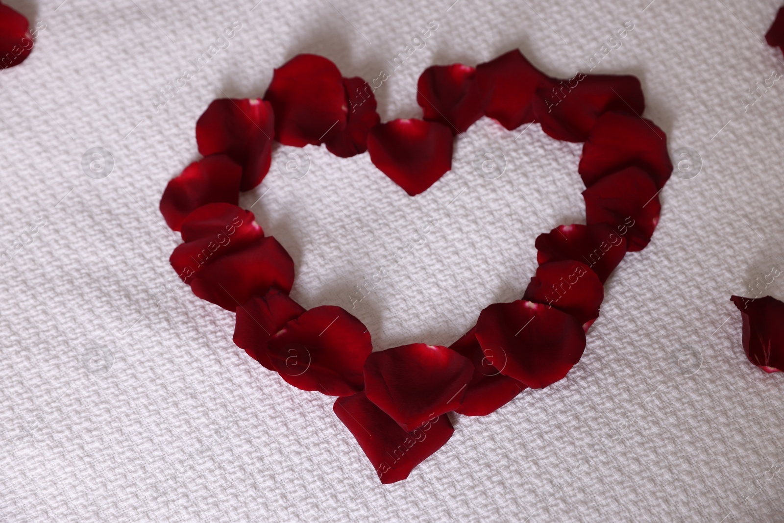Photo of Heart made with beautiful rose petals on bed, top view