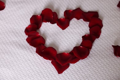 Photo of Heart made with beautiful rose petals on bed, top view
