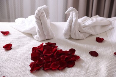 Photo of Heart of beautiful rose petals and swans made with towels on bed indoors