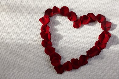Photo of Heart made with beautiful rose petals on bed, top view. Space for text