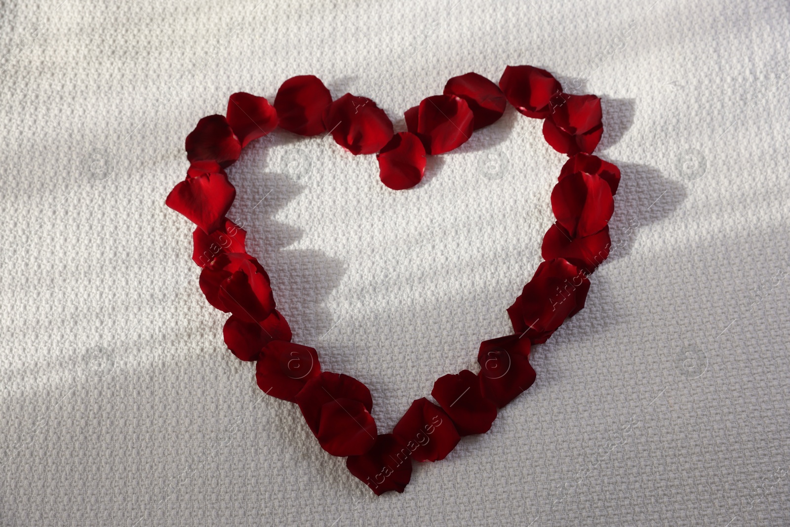 Heart made with beautiful rose petals on bed, top view Photo of Heart made with beautiful rose petals on bed, top view