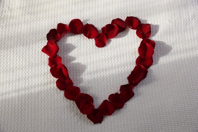 Photo of Heart made with beautiful rose petals on bed, top view