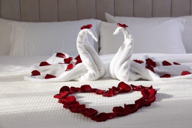 Photo of Heart of beautiful rose petals and swans made with towels on bed indoors