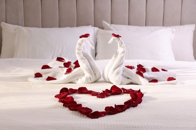Photo of Heart of beautiful rose petals and swans made with towels on bed indoors
