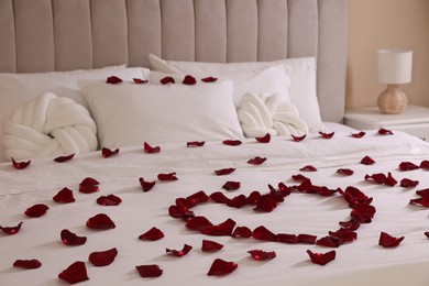 Photo of Heart made with beautiful rose petals on bed indoors