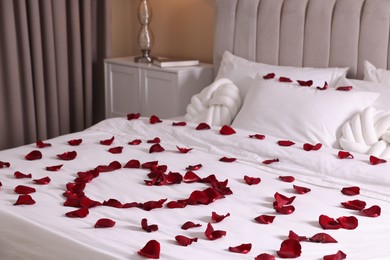 Photo of Heart made with beautiful rose petals on bed indoors