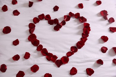Photo of Heart made with beautiful rose petals on bed, top view