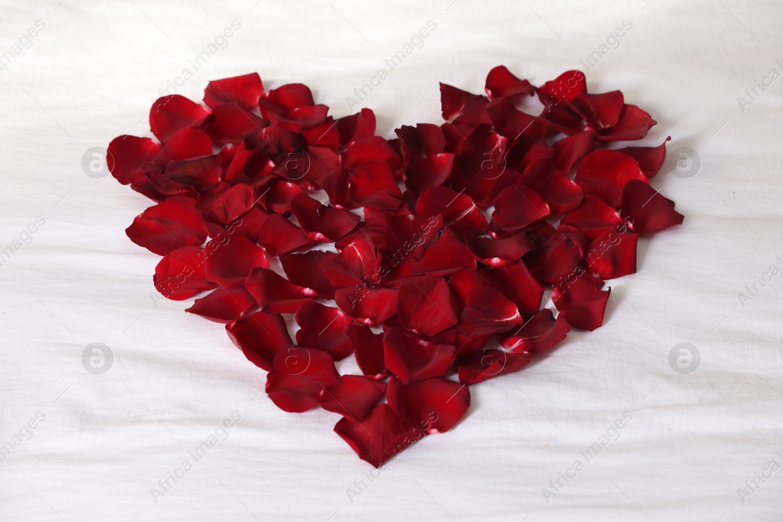 Heart made with beautiful rose petals on bed, above view Photo of Heart made with beautiful rose petals on bed, above view