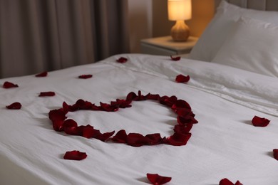 Photo of Heart made with beautiful rose petals on bed indoors