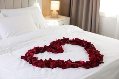 Photo of Heart made with beautiful rose petals on bed indoors