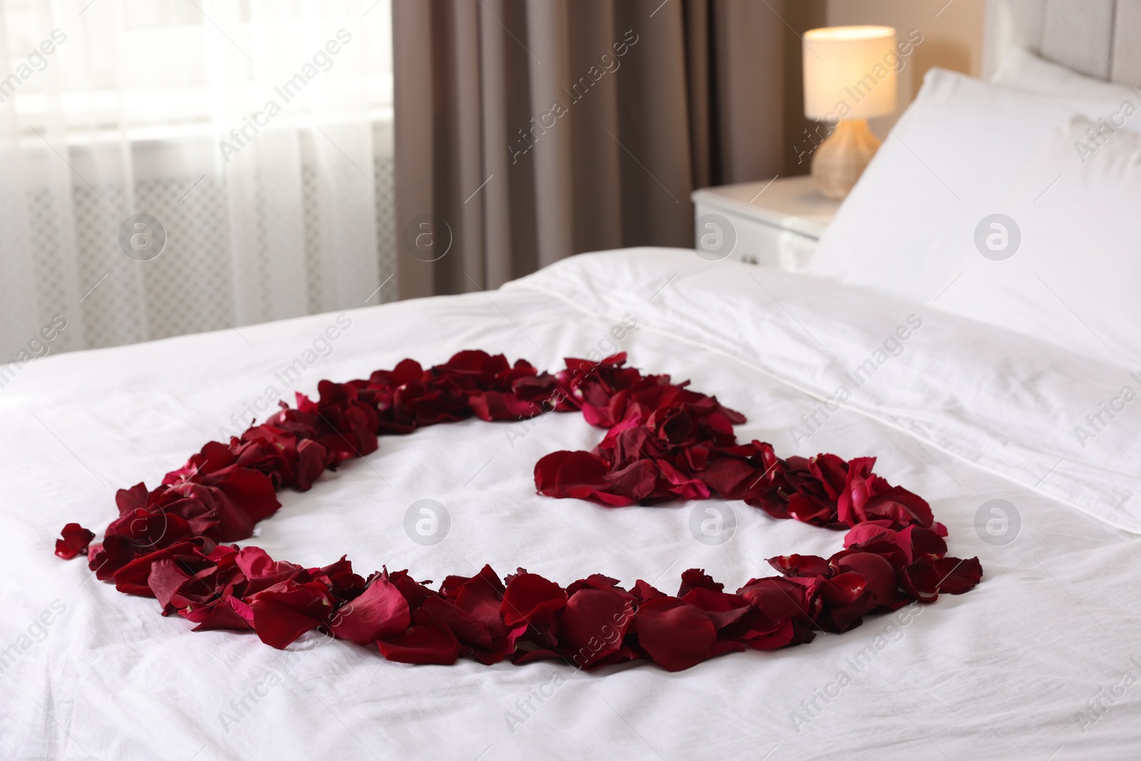 Heart made with beautiful rose petals on bed Photo of Heart made with beautiful rose petals on bed