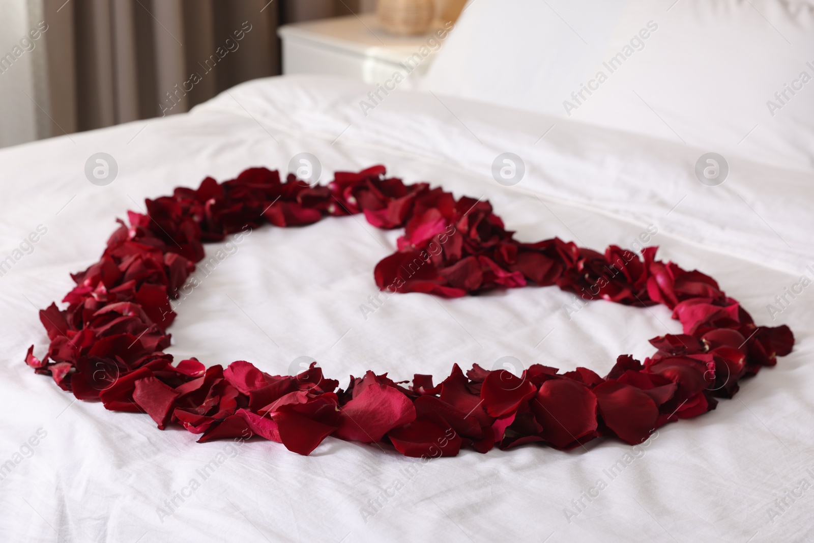 Heart made with beautiful rose petals on bed, closeup Photo of Heart made with beautiful rose petals on bed, closeup