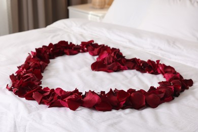 Photo of Heart made with beautiful rose petals on bed, closeup