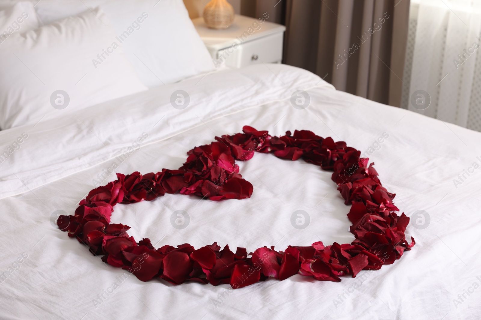 Heart made with beautiful rose petals on bed Photo of Heart made with beautiful rose petals on bed