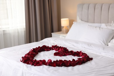 Photo of Heart made with beautiful rose petals on bed indoors
