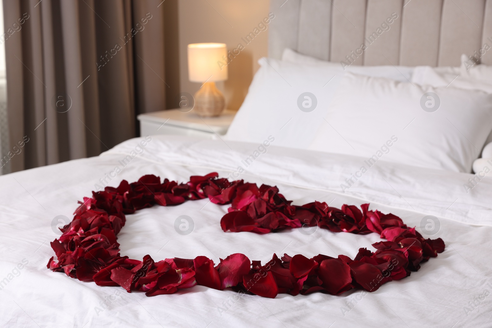Heart made with beautiful rose petals on bed indoors Photo of Heart made with beautiful rose petals on bed indoors