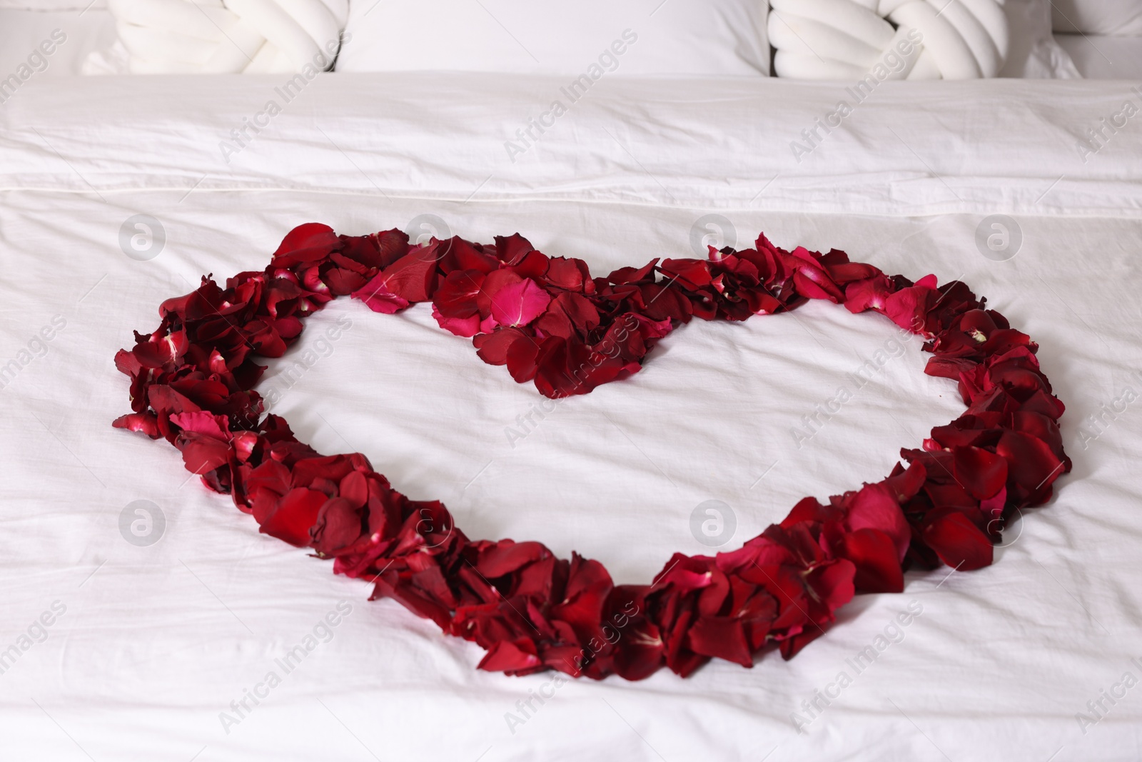 Photo of Heart made with beautiful rose petals on bed