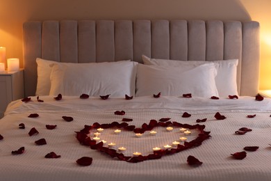 Photo of Heart made with beautiful rose petals and burning candles on bed indoors