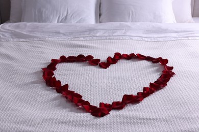 Photo of Heart made with beautiful rose petals on bed indoors