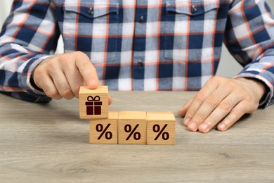 Image of Bonus. Man touching cube with gift box image among other ones with percent signs on wooden table, closeup