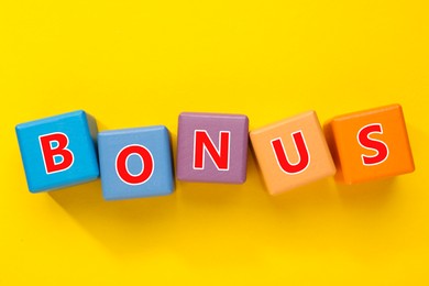 Image of Word Bonus made of colorful cubes with letters on yellow background, top view