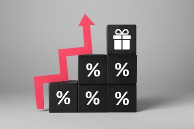 Image of Cube with gift box image on top of stacked ones with percent signs and red wooden arrow against grey background