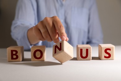 Image of Woman making word Bonus of wooden cubes with letters on table, closeup