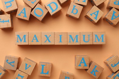 Image of Word Maximum made of wooden cubes on pale orange background, top view