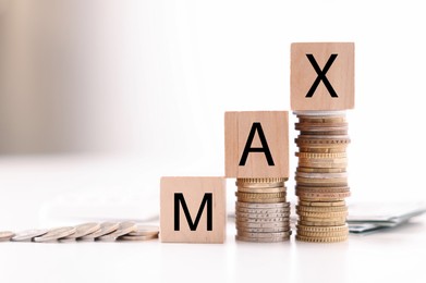 Image of Wooden cubes with word Max on stacked coins on table