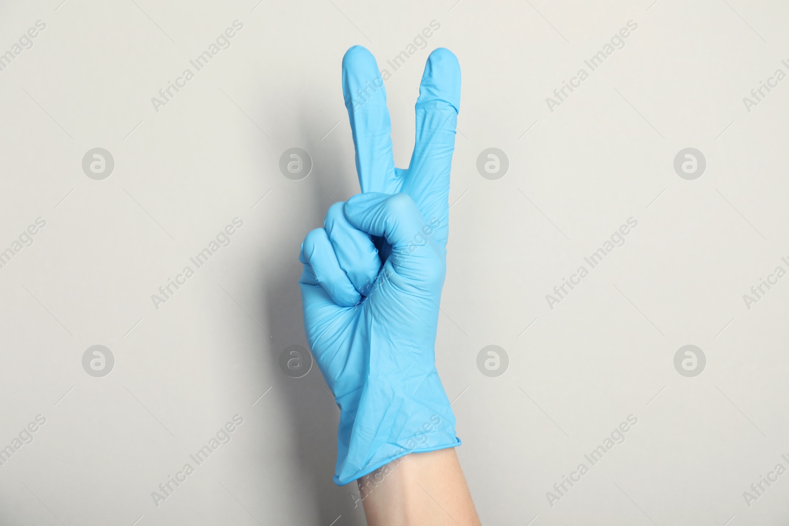 Photo of Doctor in medical glove showing two fingers on light grey background, closeup