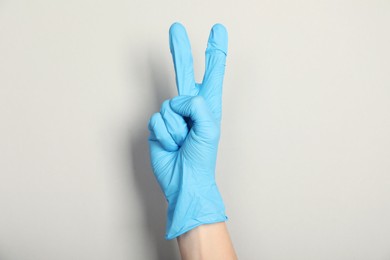 Photo of Doctor in medical glove showing two fingers on light grey background, closeup