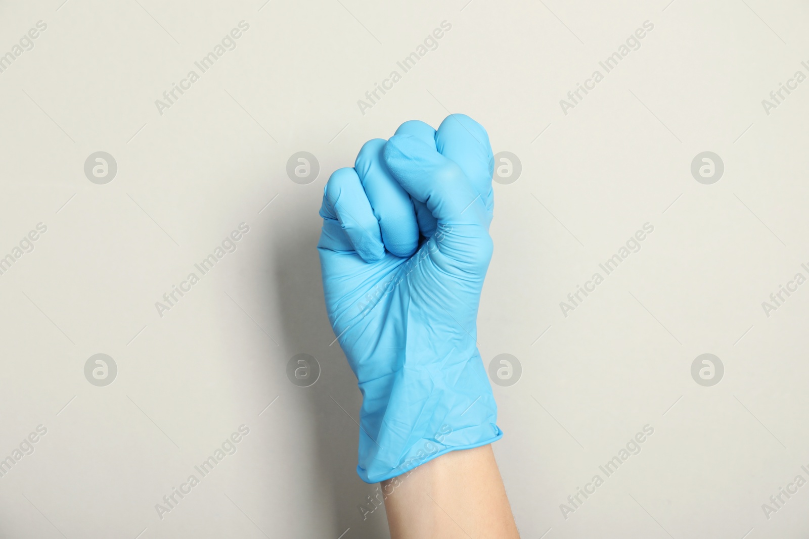 Photo of Doctor in medical glove showing fist on light grey background, closeup