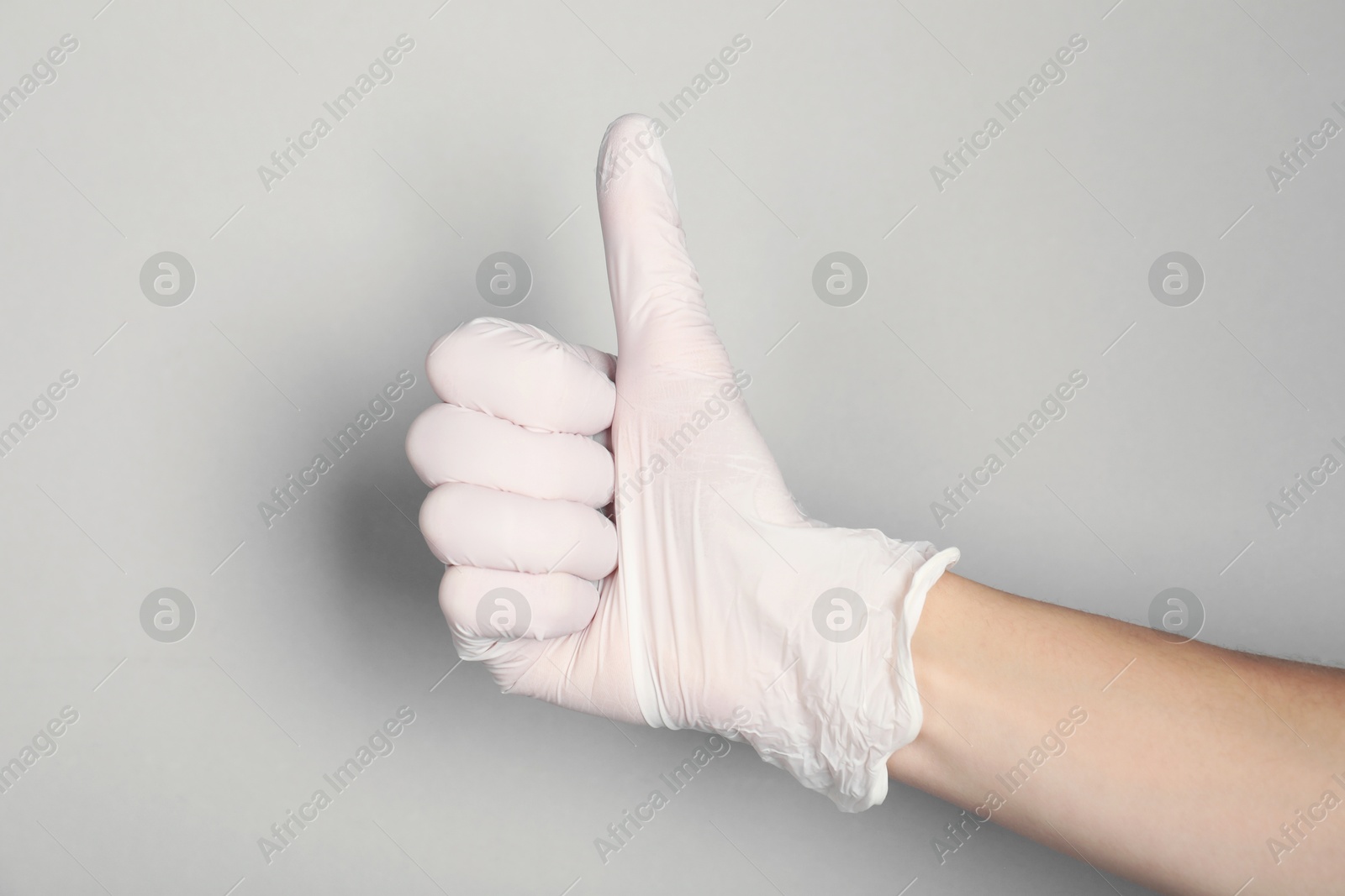 Photo of Doctor in medical glove showing thumbs up on light grey background, closeup